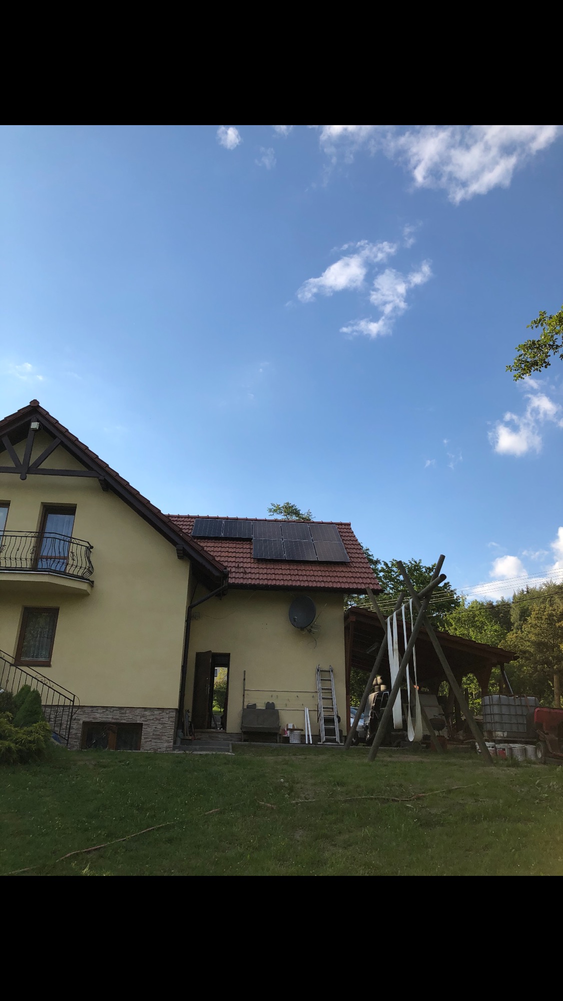 Dom jednorodzinny z zamontowanymi panelami słonecznymi na dachu z czerwonej dachówki, widoczne z poziomu trawnika w słoneczny dzień.