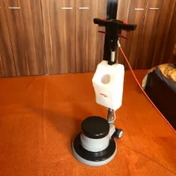 Profesjonalna maszyna czyszcząca Sprintus Ems 175 na pomarańczowym dywanie, widoczna szafa w tle.