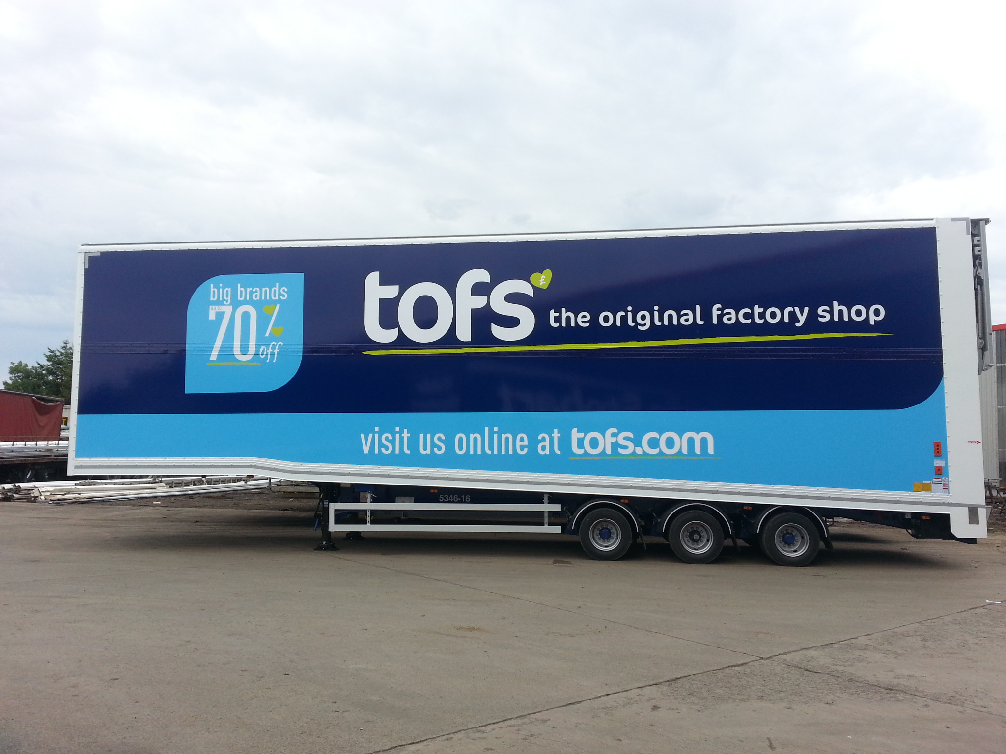 Naczepa ciężarówki z niebiesko-białym brandingiem firmy TOFS, reklamująca promocje i adres strony internetowej