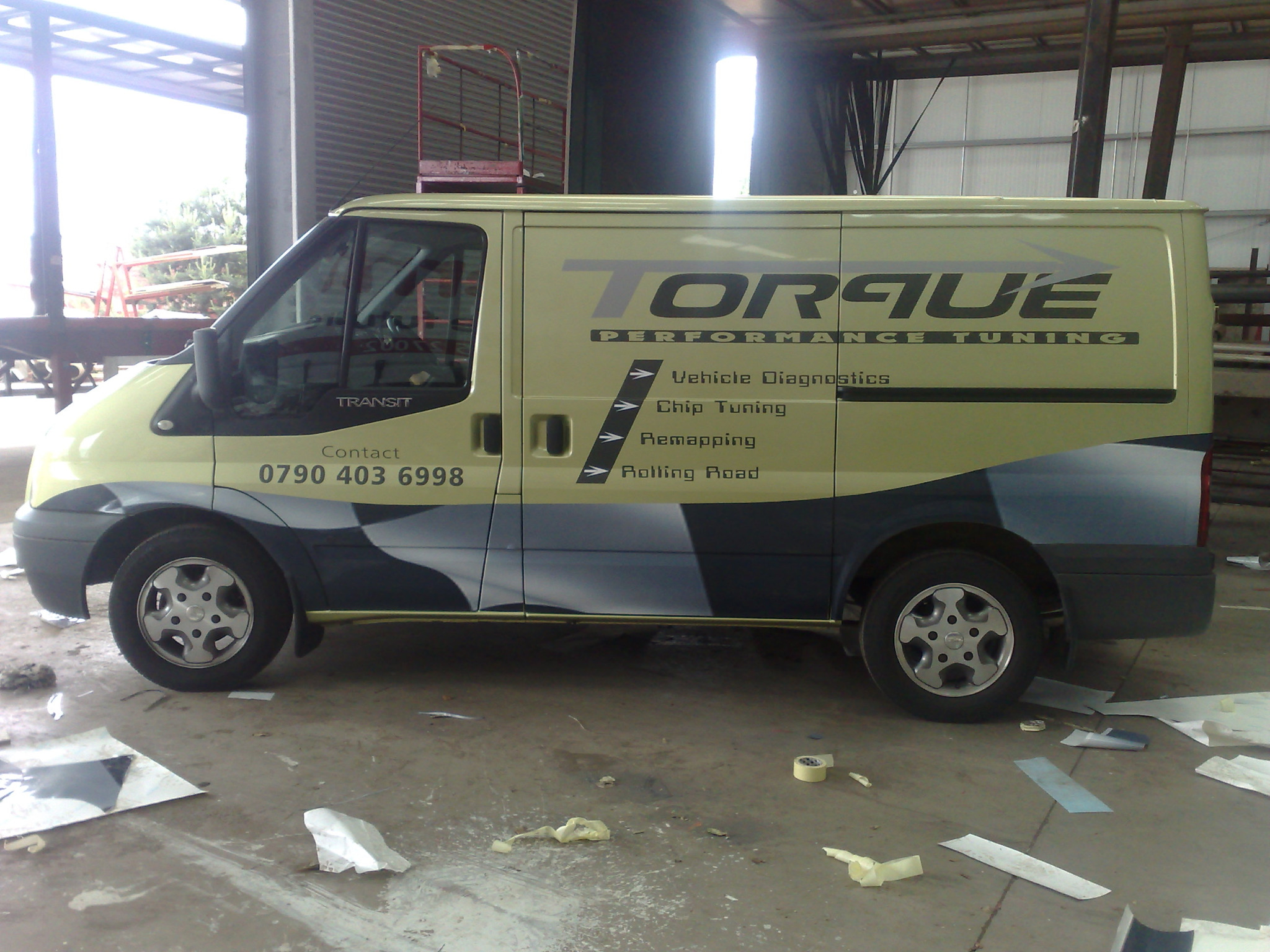 Określona okleina na samochodzie dostawczym Ford Transit z logo firmy Torque Performance Tuning oferującej diagnostykę pojazdów, chip tuning, remapowanie i hamownię, widoczne resztki folii i taśmy...