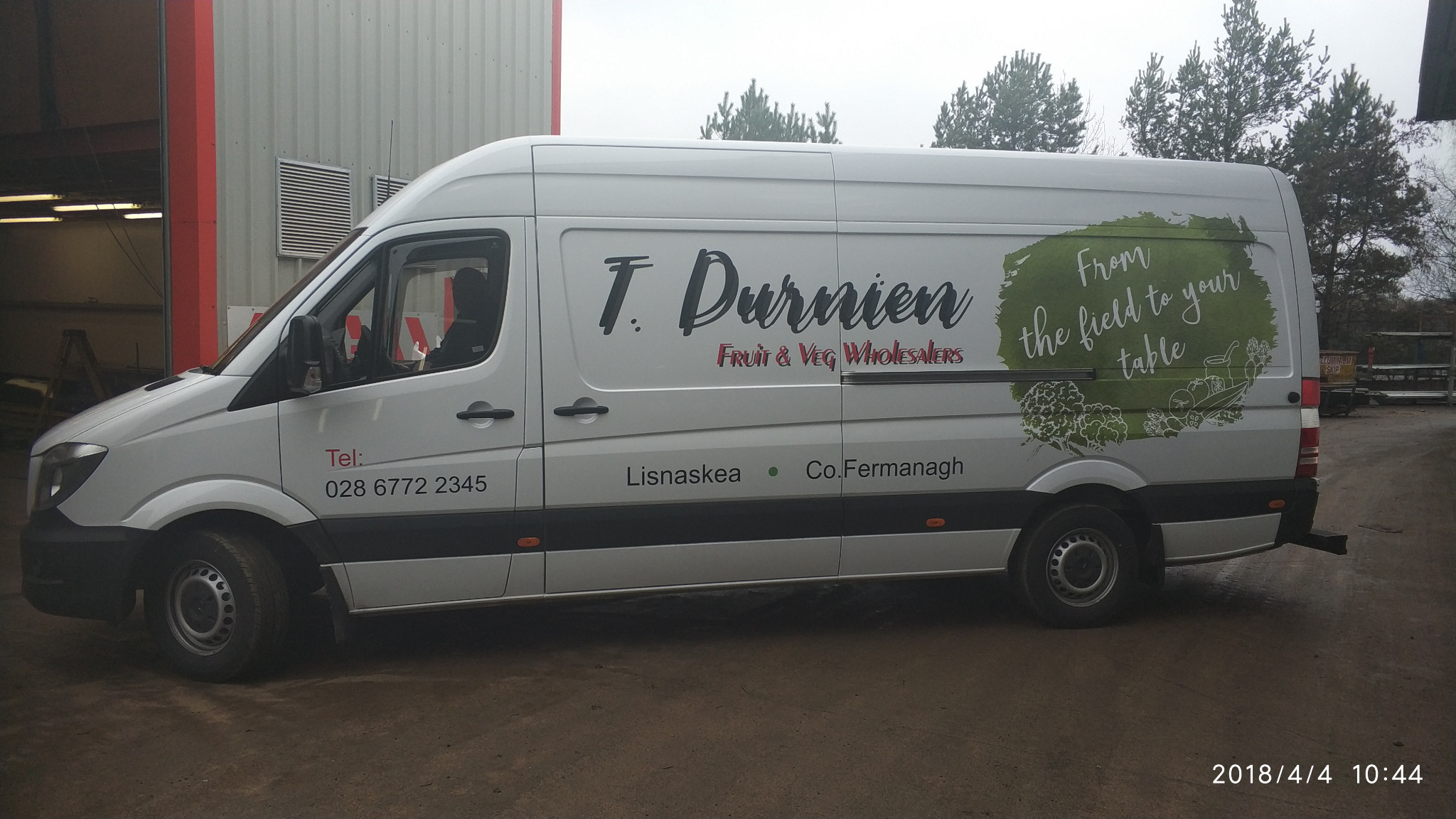 Biała furgonetka z grafiką reklamową firmy T. Durnien Fruit & Veg Wholesalers, z hasłem 'From the field to your table' i ilustracjami warzyw, zaparkowana na zewnątrz budynku.