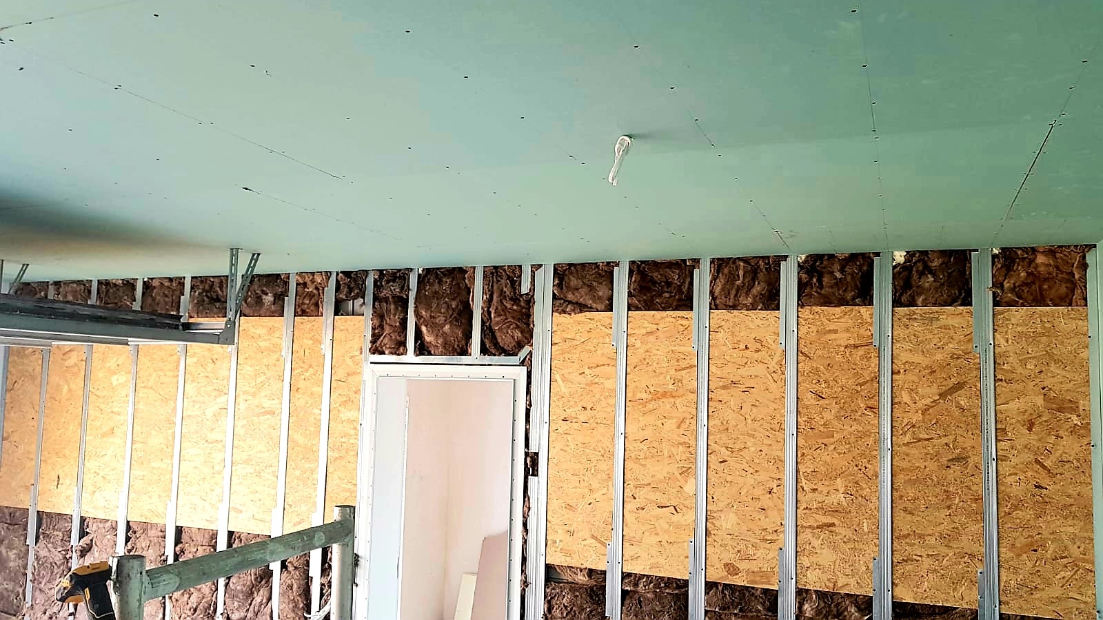 Montaż płyty karton gips na ścianie z widoczną izolacją z wełny mineralnej i konstrukcją metalową, częściowo zakryte płytami OSB, sufit z płyt karton gips.