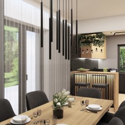 LA CASA STUDIO Iwona Wolska - Nowoczesna jadalnia z drewnianym stołem, czarnymi krzesłami i lampami wiszącymi. Widok na kuchnię z zielonymi roślinami i oknem na ogród.