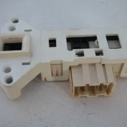 Biały, plastikowy moduł blokady drzwi z wtyczką elektryczną, prawdopodobnie element z pralki lub zmywarki, widoczne ślady użytkowania.