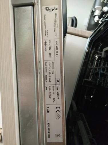Wnętrze otwartej zmywarki Whirlpool z widoczną tabliczką znamionową zawierającą dane techniczne i certyfikaty.