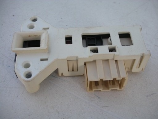 Biały, plastikowy moduł blokady drzwi z wtyczką elektryczną, prawdopodobnie element z pralki lub zmywarki, widoczne ślady użytkowania.