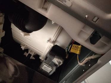 Wnętrze uszkodzonej zmywarki, widoczne elementy konstrukcyjne, przewody i plastikowe obudowy. Żółta etykieta z napisem EAD62.