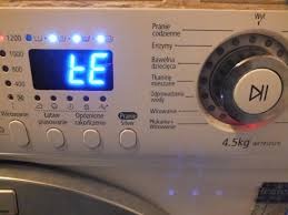 Panel sterowania pralki z wyświetlaczem wskazującym błąd 'ŁE' oraz ustawieniami programów prania.