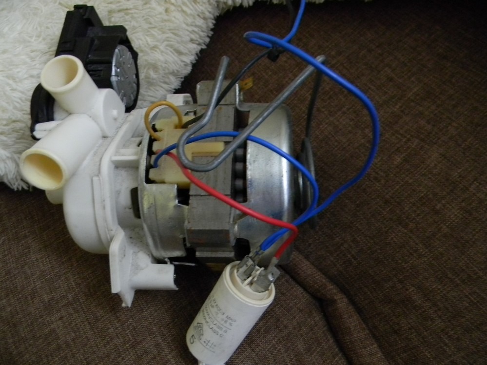 Pompa z silnikiem i kondensatorem zdemontowana z urządzenia AGD, widoczne przewody elektryczne i elementy mocujące.