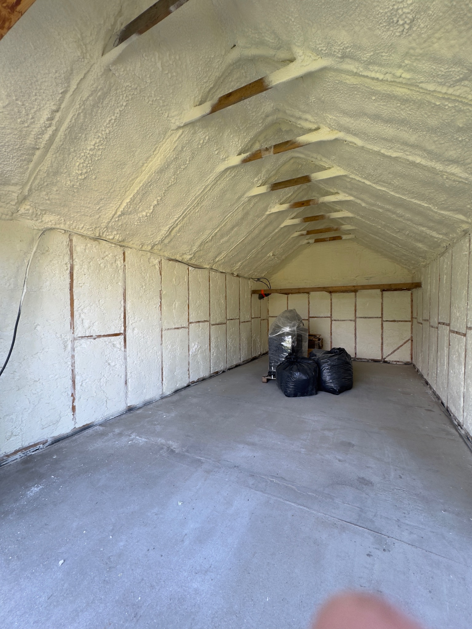 Poddasze po natrysku izolacji. Widoczne drewniane elementy konstrukcyjne i szczelna warstwa piany. Na podłodze worki z odpadami po aplikacji.