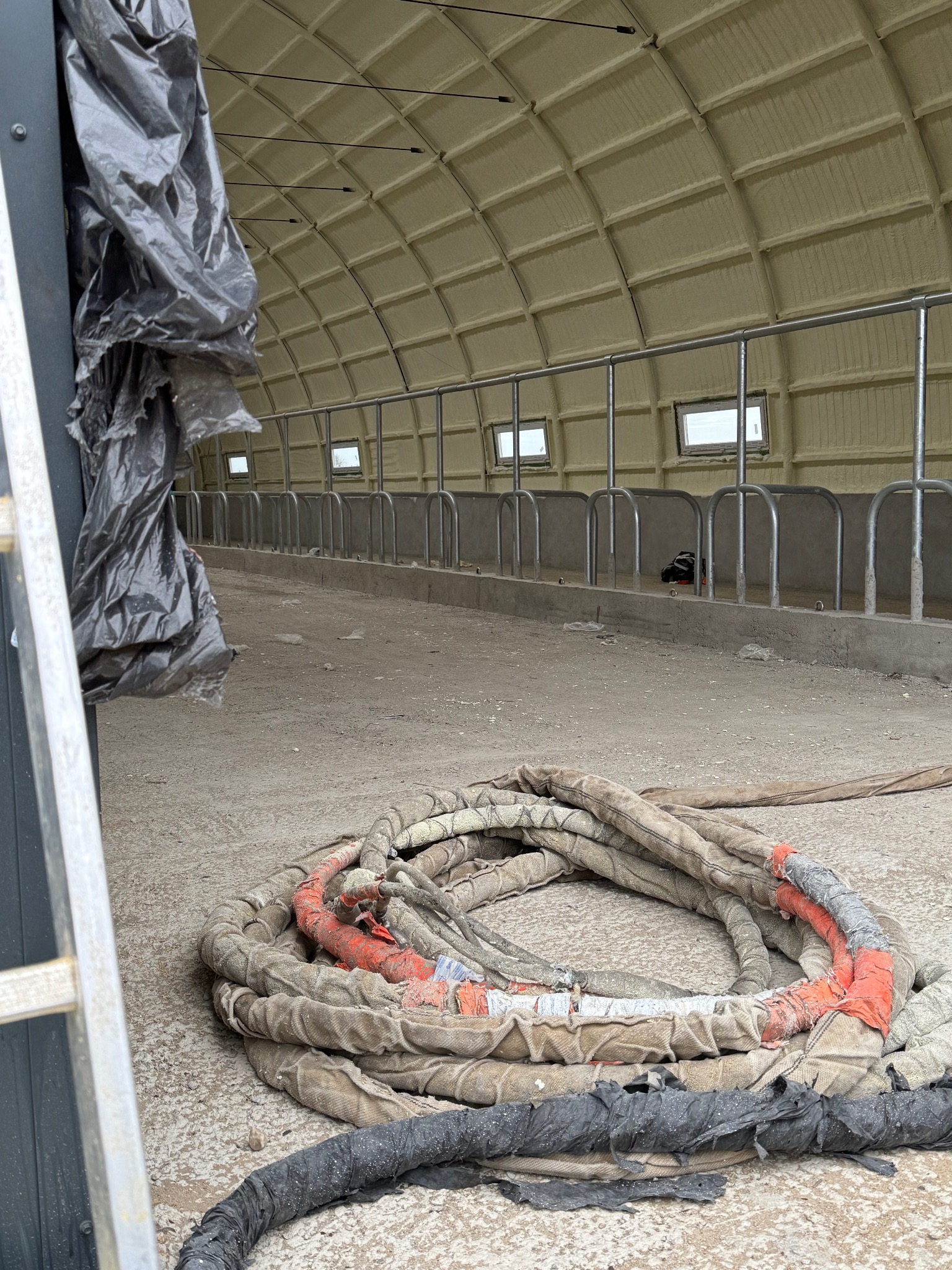 Ocieplony pianką PUR strop w hali, widoczne narzędzia pracy: wąż do piany, drabina i folia ochronna. Detal z bliska ukazuje strukturę piany na suficie.