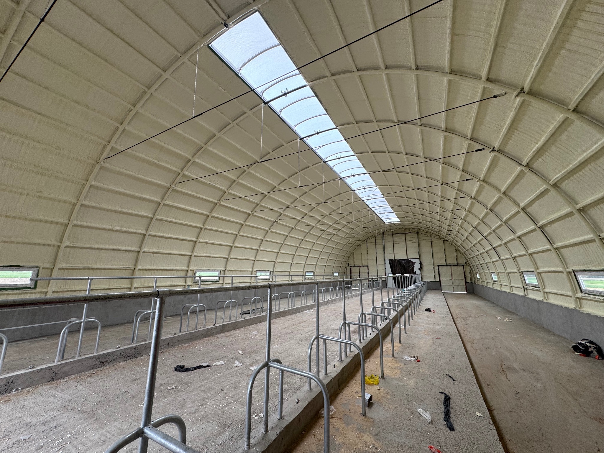 Wnętrze hali rolniczej po natrysku izolacji. Widoczne ocieplone ściany i sufit z oknami dachowymi. Metalowe konstrukcje wewnątrz. Jasna, równomierna warstwa izolacji.