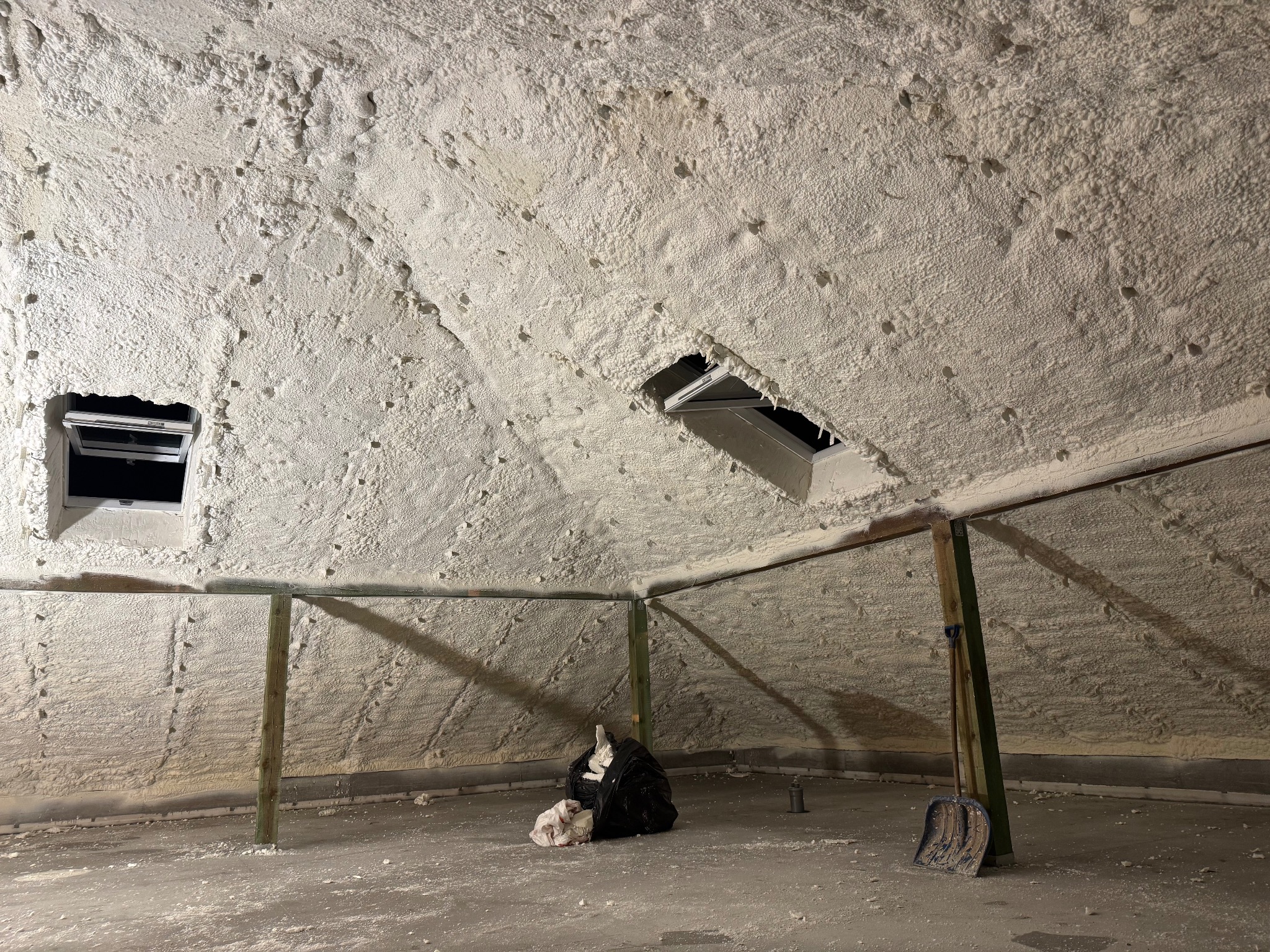 Poddasze po ociepleniu pianką PUR: widoczne okna dachowe, drewniane podpory i resztki piany na podłodze. Izolacja natryskowa wykonana wewnątrz budynku.