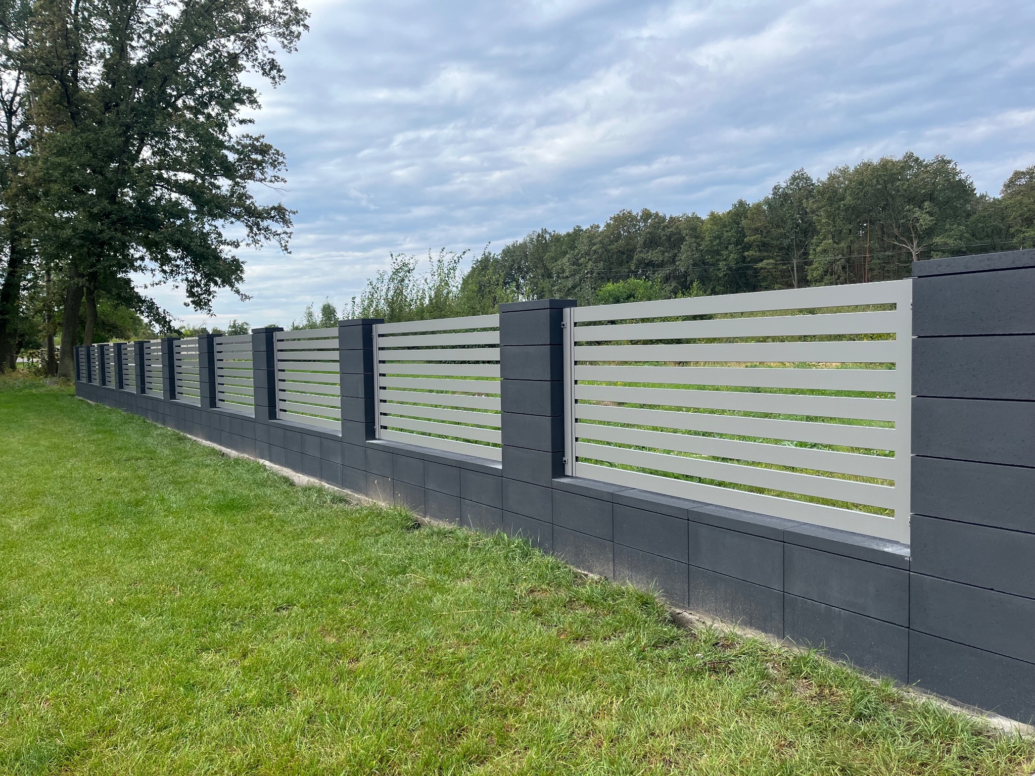 Nowoczesne ogrodzenie z poziomych, białych przęseł i grafitowych słupków z bloczków betonowych, otoczone zielonym trawnikiem, Nowa Sól.