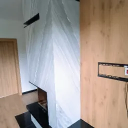 Nowoczesny kominek obudowany płytami z szarego marmuru z białymi żyłami, z czarnym, błyszczącym blatem i drewnianą ścianą w tle, z zamontowanym uchwytem do telewizora.