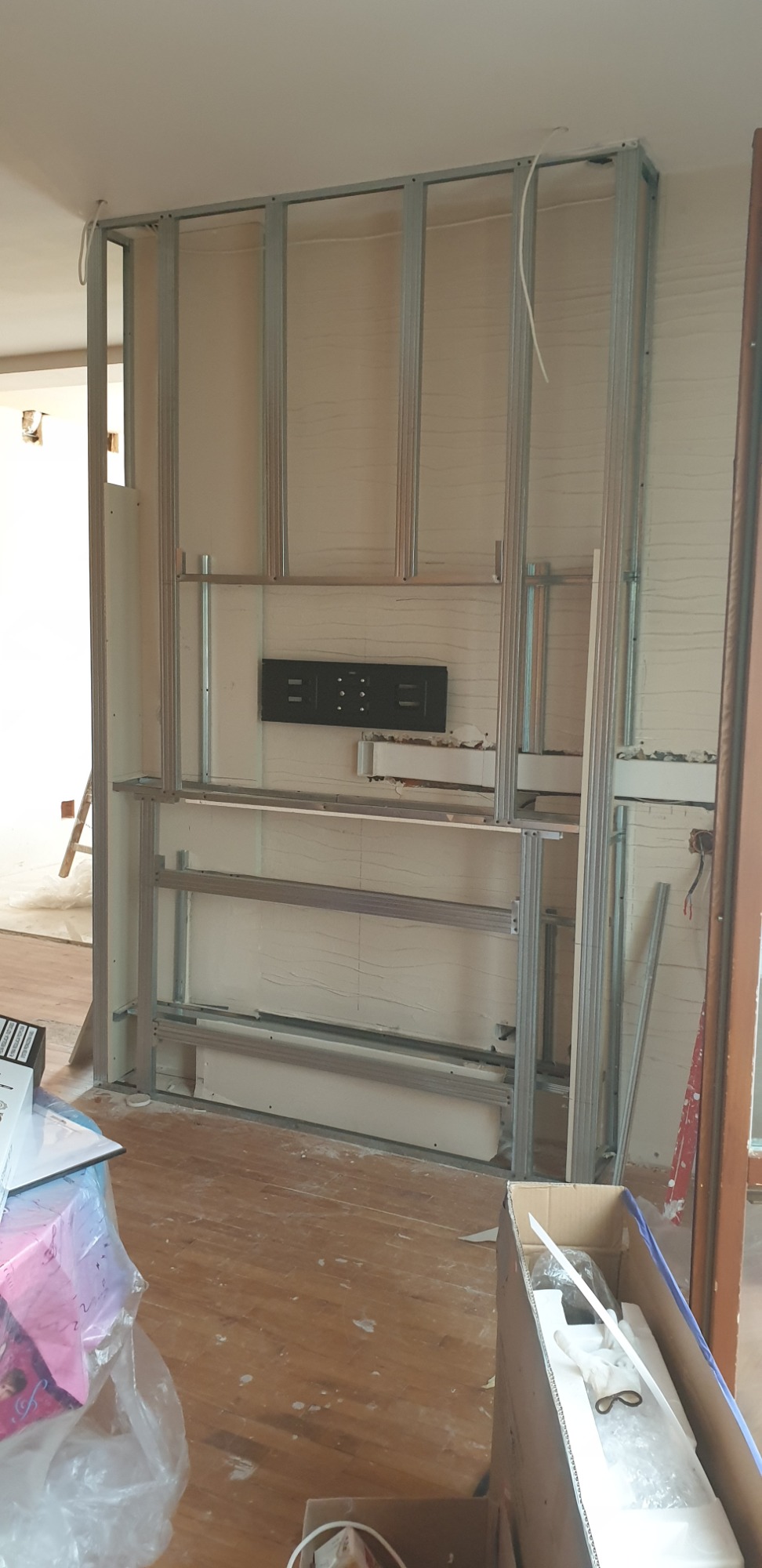 Konstrukcja metalowa ściany działowej z zamontowanym uchwytem na telewizor, przygotowana do obłożenia płytami, widoczna w pomieszczeniu w trakcie remontu w Nowym Targu. Na podłodze widoczne ślady...