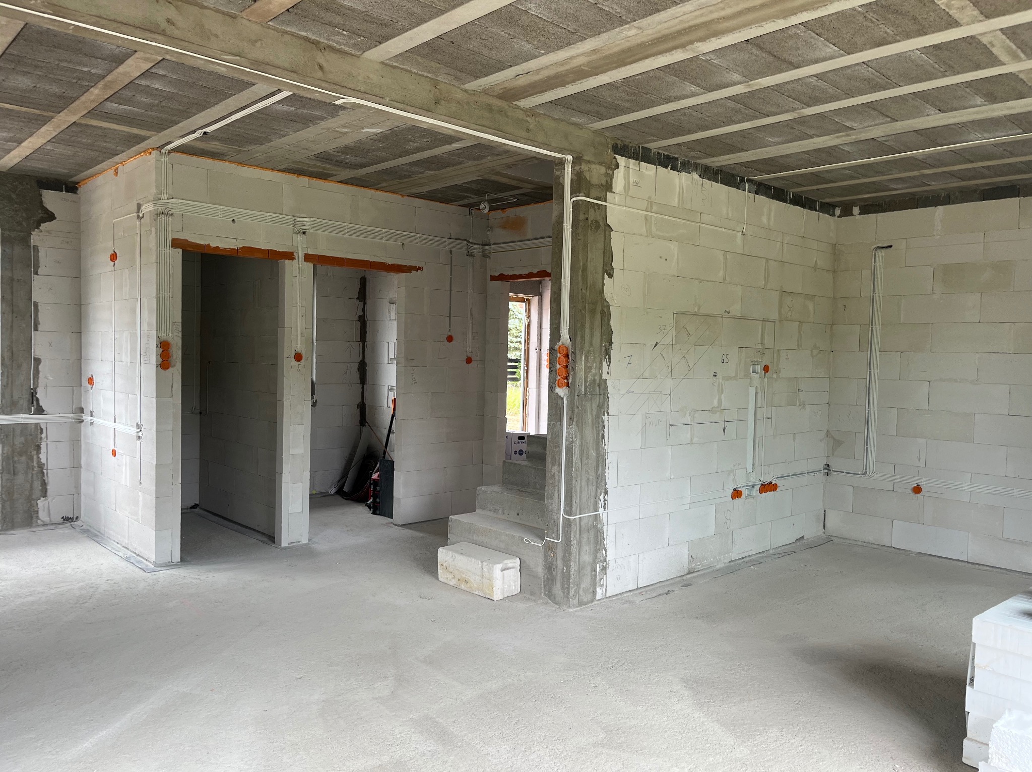 Surowy stan wnętrza z instalacją elektryczną: widoczne puszki i przewody na ścianach z betonu komórkowego, sufit z prefabrykatów. Okno w tle.