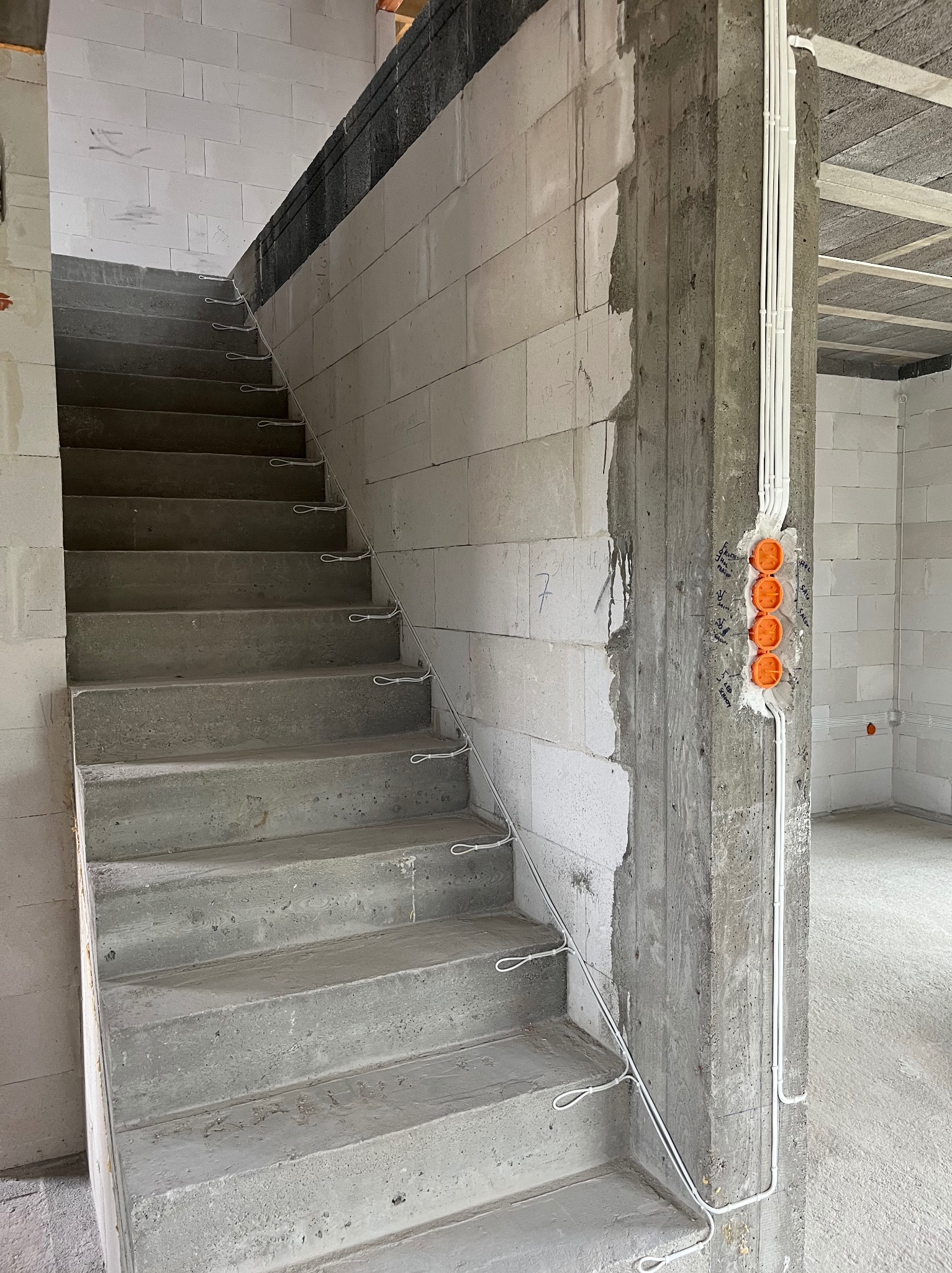 Surowe schody betonowe w nowym budynku z widoczną instalacją elektryczną w peszlach i puszkami podtynkowymi w ścianie z betonu komórkowego.