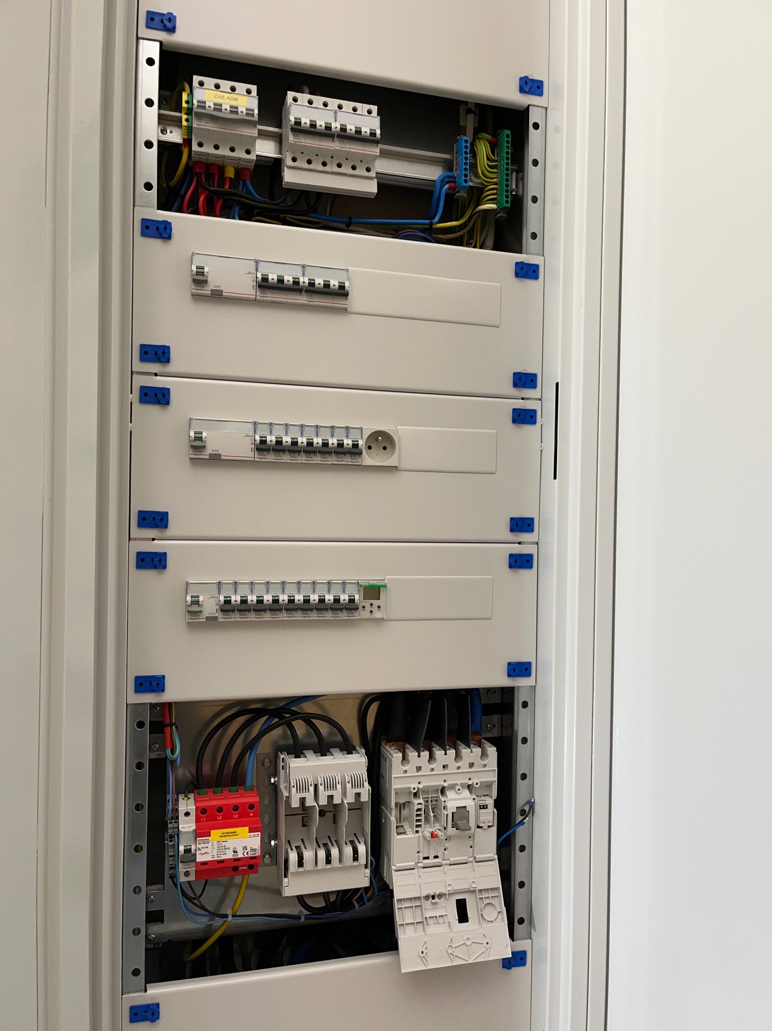 Rozdzielnica elektryczna z modułami, zabezpieczeniami i gniazdem. Widoczne przewody, listwy DIN i elementy mocujące. Oświetlenie równomierne, neutralne tło.