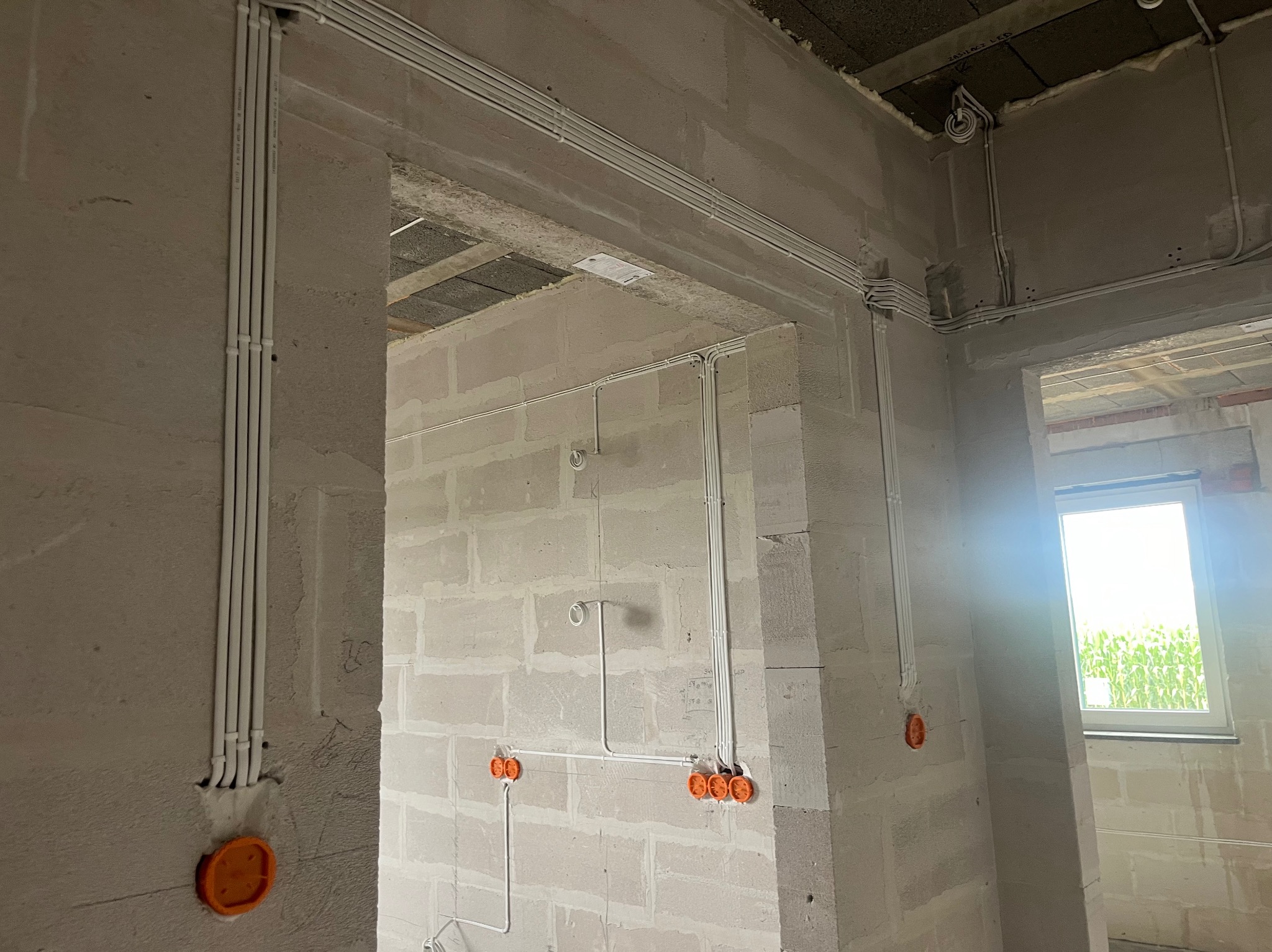 Białe kable elektryczne prowadzone po ścianach z betonu komórkowego w surowym wnętrzu budynku. Widoczne pomarańczowe puszki instalacyjne.
