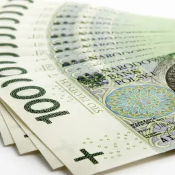 Rozłożony wachlarz banknotów 100 złotych na białym tle, widoczne detale nominału i wizerunku króla.