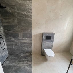 DB Dawid Bojarski - Nowoczesna łazienka z kabiną prysznicową typu walk-in wyłożoną szarymi płytkami imitującymi marmur, kontrastującymi z jasnymi płytkami na pozostałej powierzchni. Czarna armatura prysznicowa...