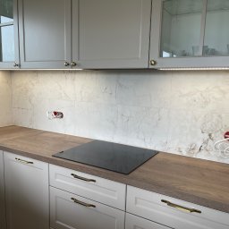 DB Dawid Bojarski - Wykończona kuchnia z marmurową ścianą, drewnianym blatem, indukcyjną płytą i szarymi szafkami z oświetleniem LED podszafkowym, widoczne gniazdka elektryczne przed podłączeniem.