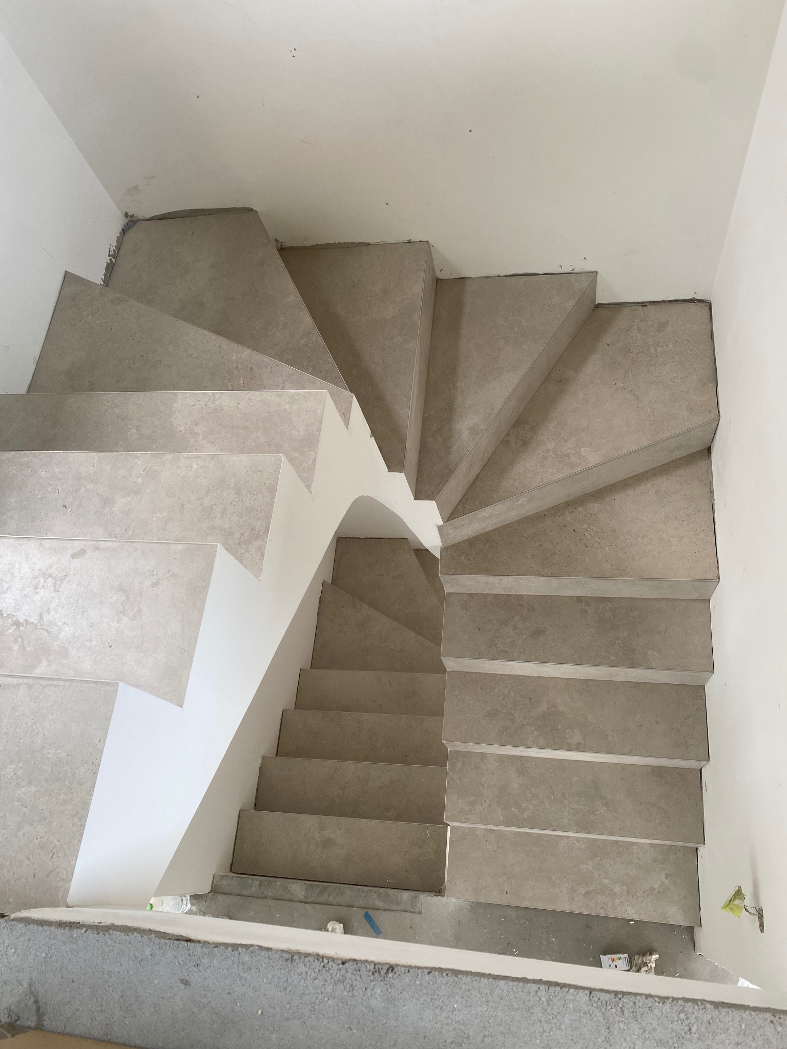 Wewnętrzne schody spiralne z szarych, marmurkowych płytek, widok z góry, białe ściany w tle, etap wykończeniowy.
