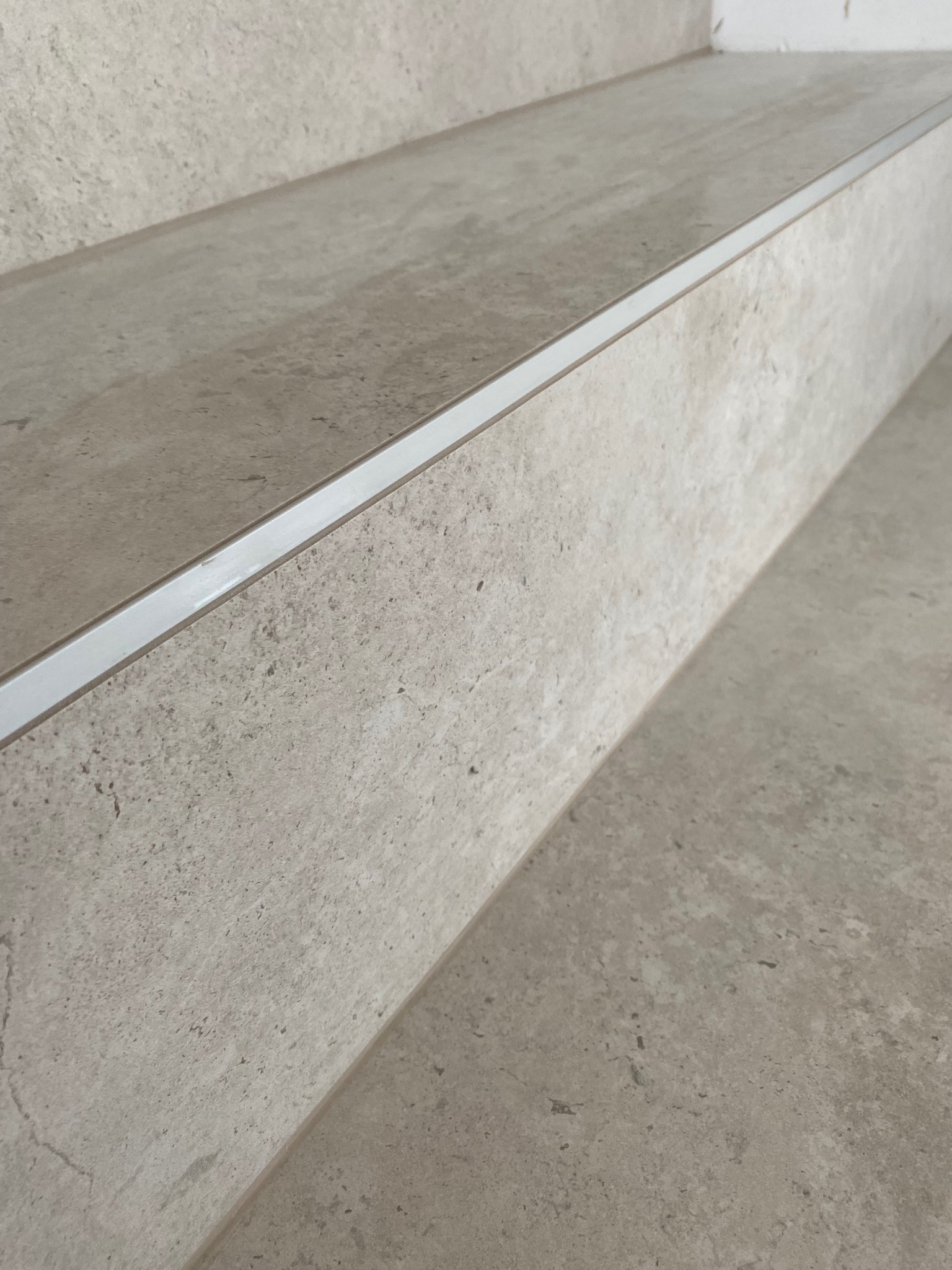 Wykończone schody wewnętrzne z szarego kamienia z aluminiową listwą zabezpieczającą krawędzie stopni.