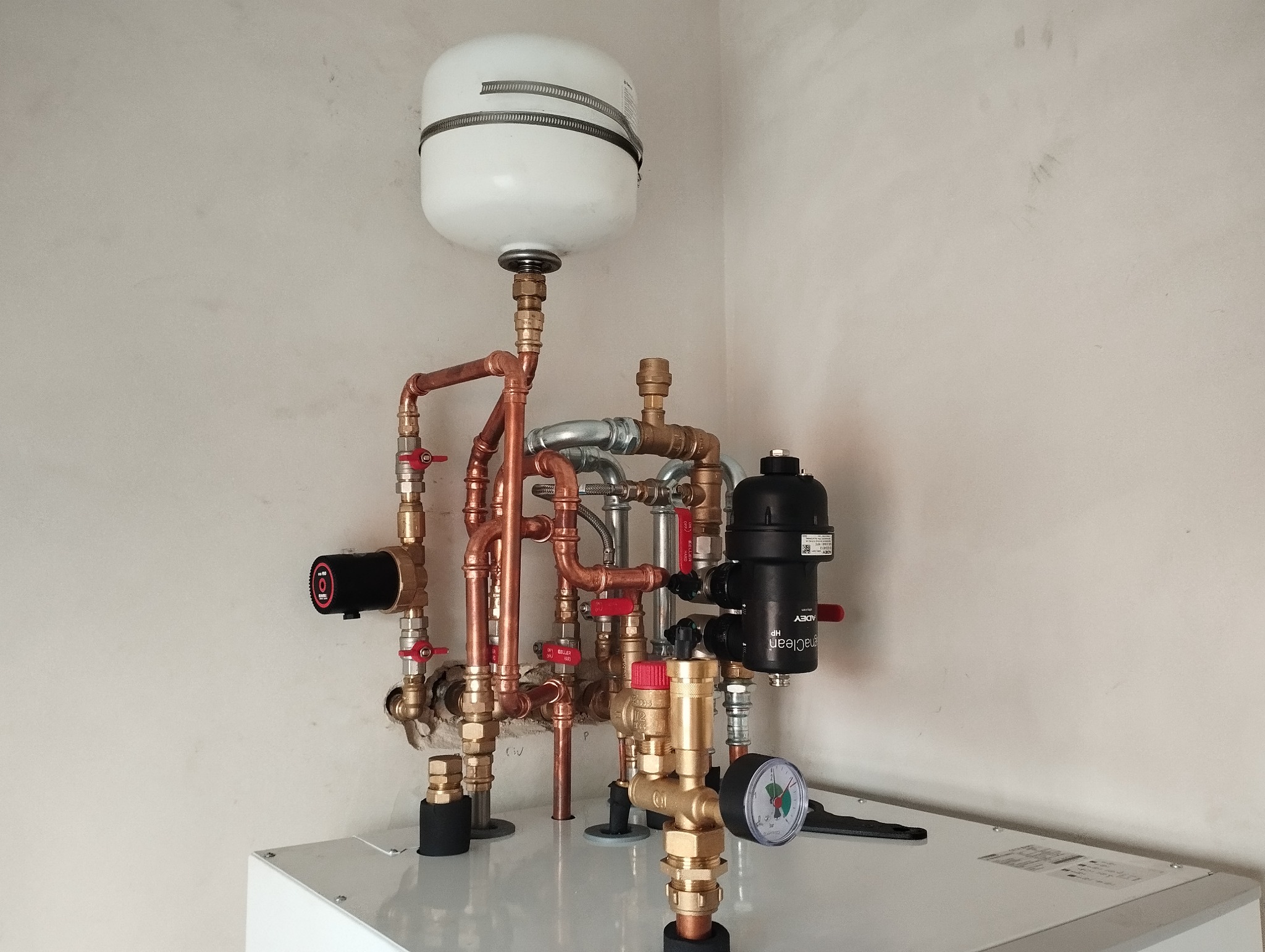 Złożona instalacja grzewcza z zbiornikiem wyrównawczym, pompą obiegową, filtrem magnetycznym i manometrem, wykonana z rur miedzianych i elementów mosiężnych, zamontowana na kotle grzewczym przy...