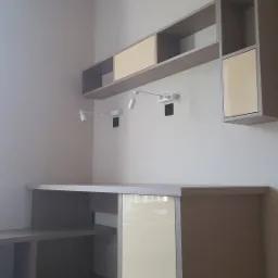 Szaro-beżowe biurko z szafkami i półkami wiszącymi, z oświetleniem punktowym, nowoczesny design, drewniana podłoga.