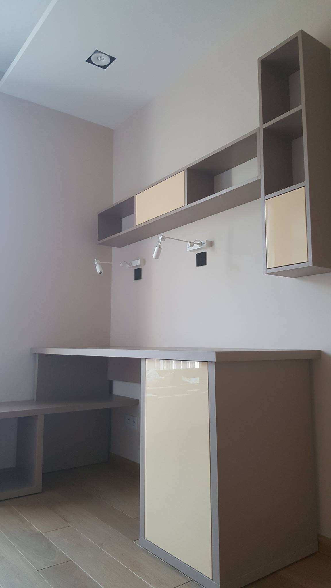 Szaro-beżowe biurko z szafkami i półkami wiszącymi, z oświetleniem punktowym, nowoczesny design, drewniana podłoga.