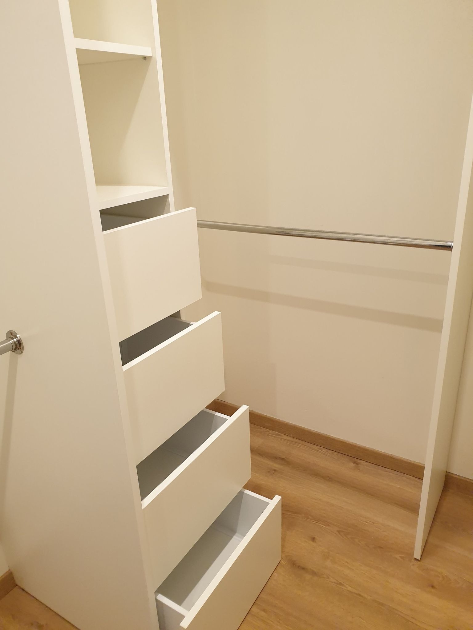 Wnętrze garderoby z białymi półkami i szufladami, jedna szuflada wysunięta, widoczny drewniany panel podłogowy.