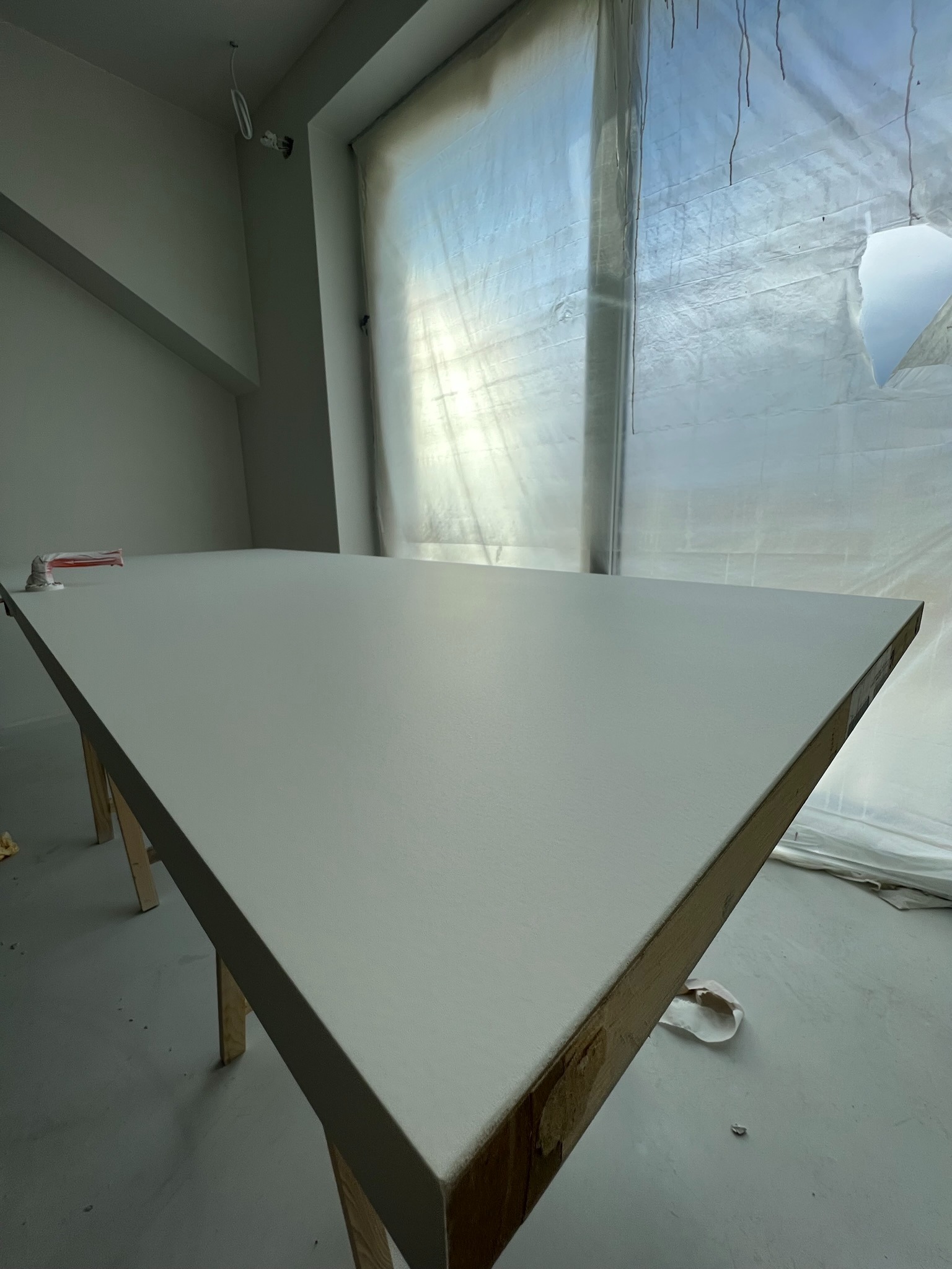 Świeżo pomalowany sufit w pomieszczeniu z oknem zabezpieczonym folią malarską, widoczny fragment narzędzia malarskiego. Praca po malowaniu.