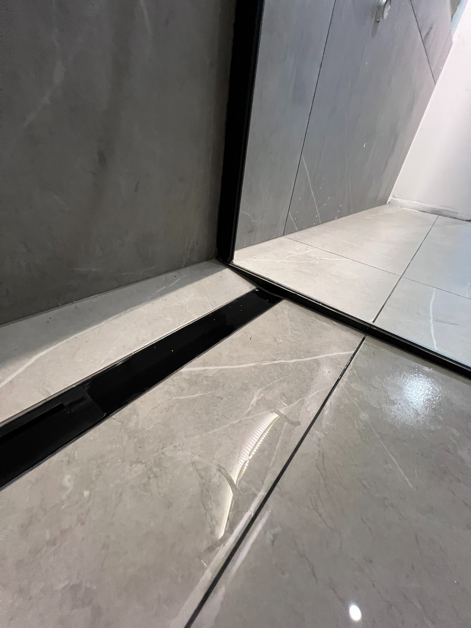 Nowoczesna łazienka z szarymi płytkami imitującymi marmur i czarnym odpływem liniowym. Minimalistyczny design, eleganckie wykończenie podłogi i ścian.