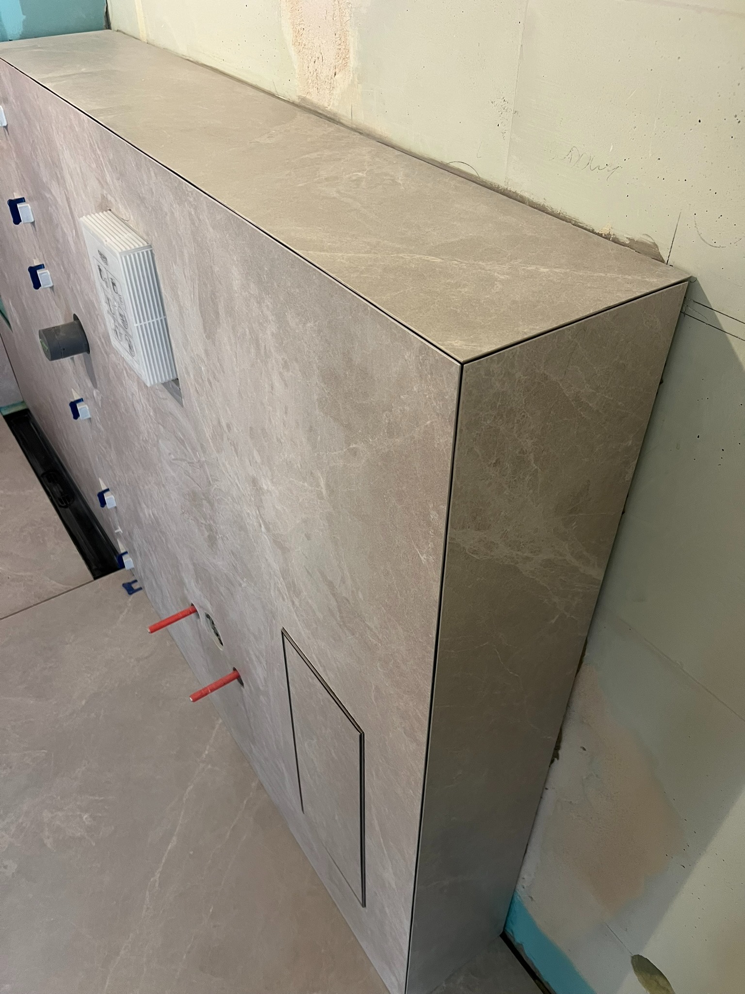 Obudowa stelaża WC z płytek imitujących marmur, widoczne elementy instalacji. Minimalistyczne wykończenie łazienki z ukrytą rewizją.