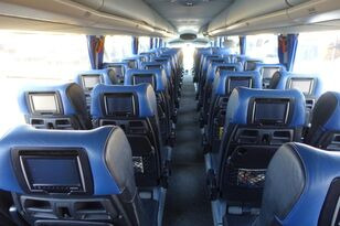 Wnętrze autobusu turystycznego z niebieskimi fotelami wyposażonymi w ekrany LCD dla pasażerów, widok wzdłuż korytarza.