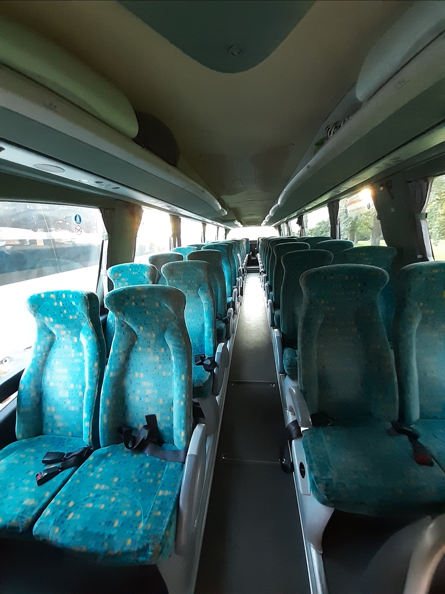 Wnętrze autobusu turystycznego z rzędami turkusowych foteli z pasami bezpieczeństwa, widok z przodu na puste przejście