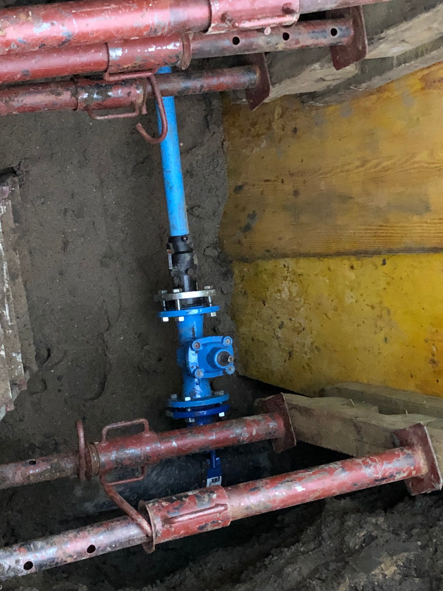 Niebieska rura z zaworem, element instalacji wodociągowej w wykopie zabezpieczonym deskami i stemplami, teren budowy w Łomiankach.