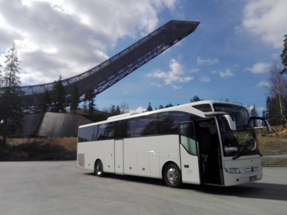 Biały autokar turystyczny z otwartymi drzwiami na tle skoczni narciarskiej Holmenkollen w Oslo, Norwegia.