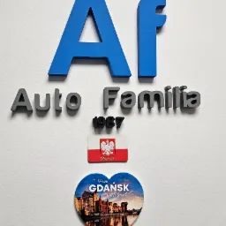 Ściana z logo firmy Auto Familia z Gdańska, rok założenia 1987, ozdobiona magnesem z flagą Polski i magnesem w kształcie serca z panoramą Gdańska.