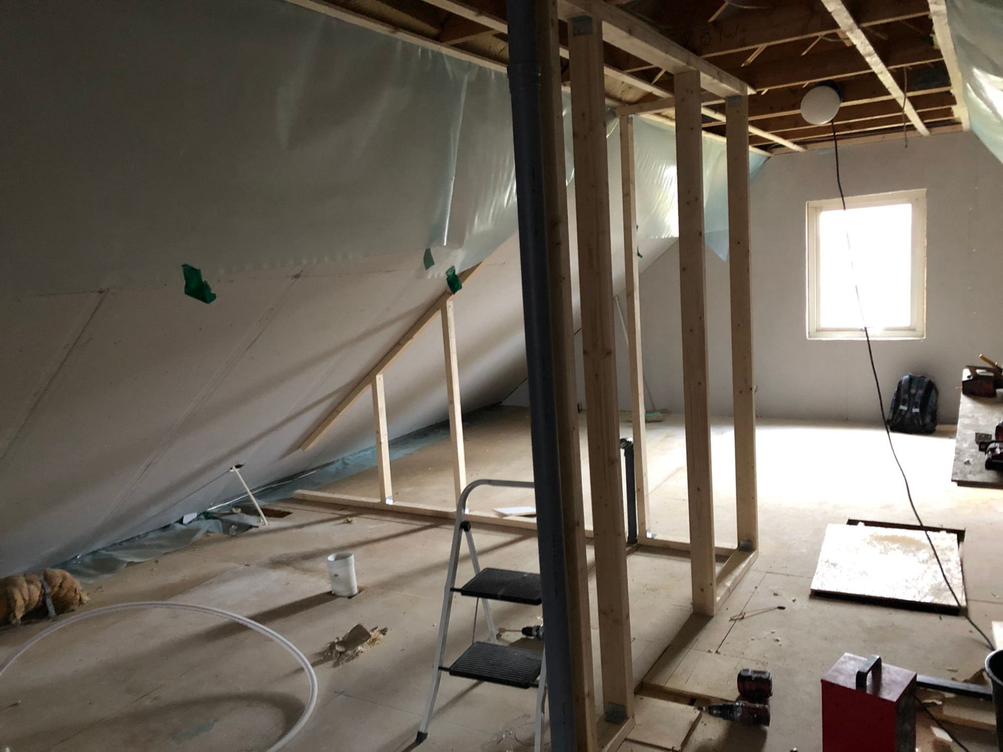 Poddasze w trakcie adaptacji: drewniana konstrukcja ścian działowych, zabezpieczona folią skośna ściana, drabina i narzędzia na podłodze.