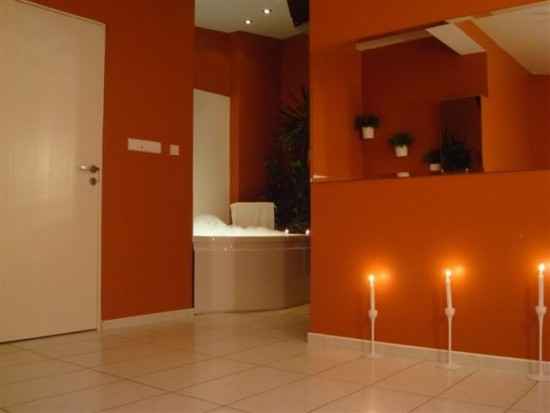 Pomarańczowa łazienka z wanną z hydromasażem, oświetlona świecami w białych świecznikach, widok z perspektywy drzwi.