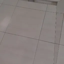 Ułożone jasne płytki podłogowe w łazience z liniowym odpływem. Widoczne fugi i detale wykończenia.