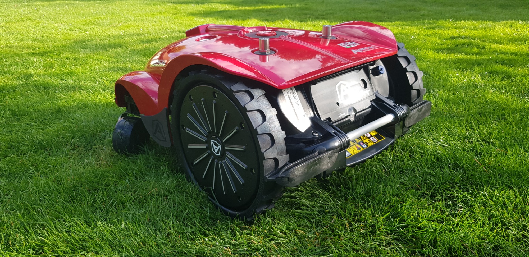 Czerwony autonomiczny robot koszący trawnik, model l250i, na tle soczystej zielonej trawy w słoneczny dzień.