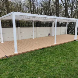 Biała, metalowa pergola z lamelowym dachem na tarasie z desek kompozytowych, widok na ogród z trawnikiem i ogrodzeniem.