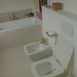 Nowoczesna łazienka w Częstochowie z białą armaturą: wanna, bidet i toaleta, minimalistyczny design, jasne płytki na podłodze i ścianach.