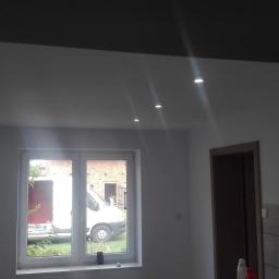 uslugi ogolnobudowlane MATEK - Wnętrze po remoncie: białe ściany, wstawione okno z widokiem na zaparkowany biały samochód dostawczy, zamontowane oświetlenie sufitowe punktowe i fragment wykończonej płytkami ściany.