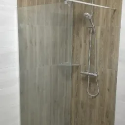 Kabina prysznicowa walk-in z odpływem liniowym, wykończona płytkami imitującymi drewno i marmur, z chromowaną armaturą.