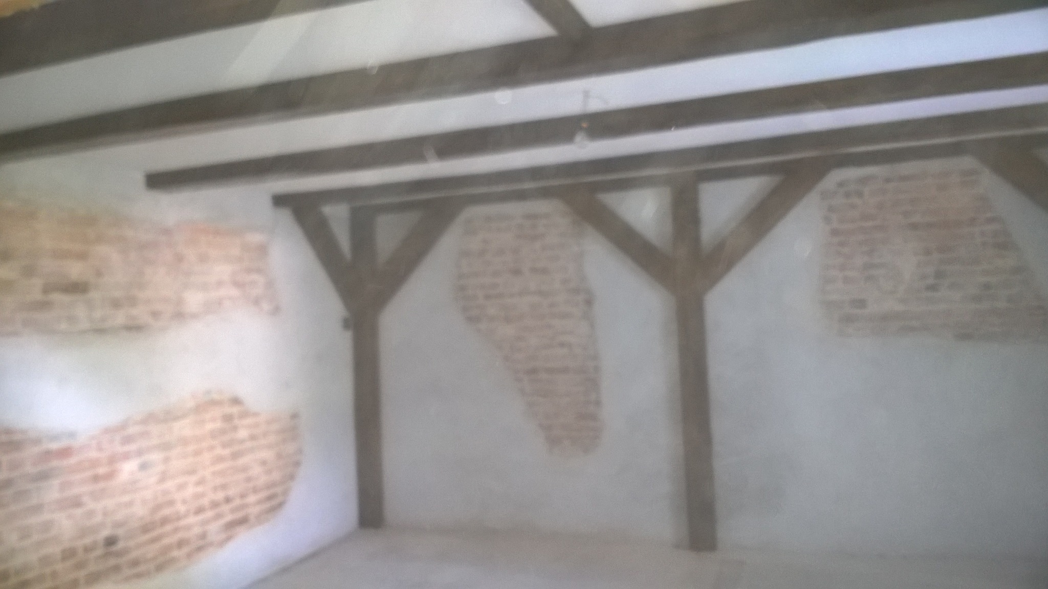 Wnętrze w trakcie prac, surowa ściana z odsłoniętą cegłą, drewniane belki stropowe i konstrukcja wsporcza, częściowo otynkowane ściany.